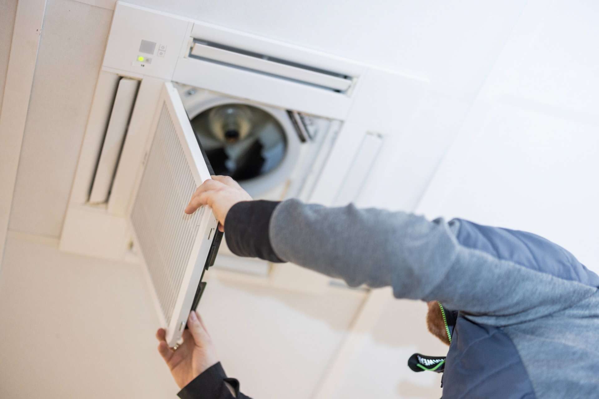 Håndværker arbejder med de indvendige mekanismer i et ventilationssystem i loftet.